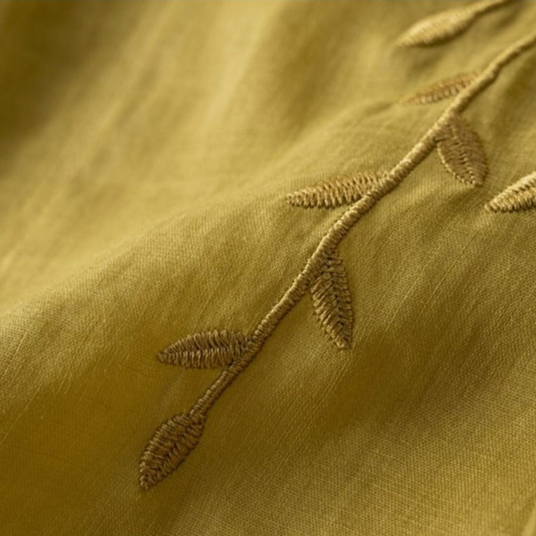 Detailed view of green fabric with fine leaf embroidery, emphasizing texture and stitchwork.