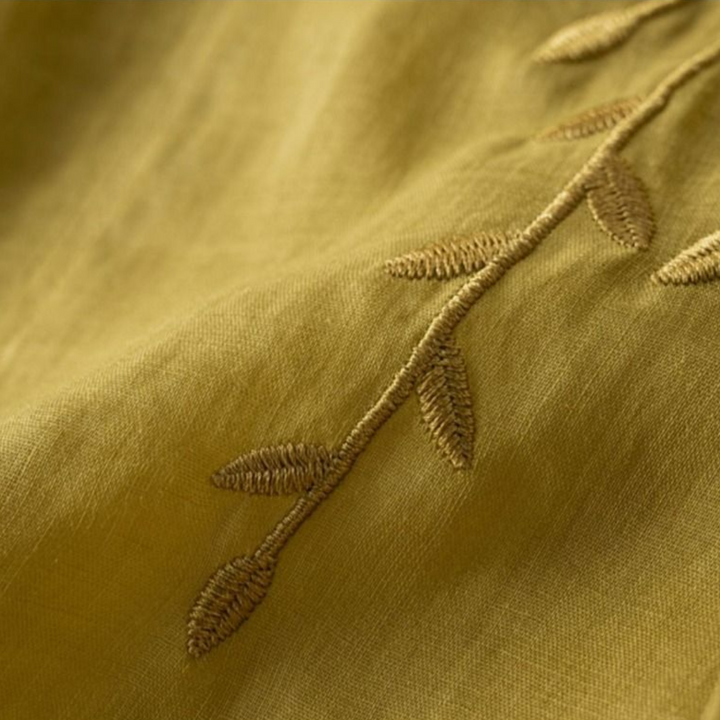 Detailed view of green fabric with fine leaf embroidery, emphasizing texture and stitchwork.