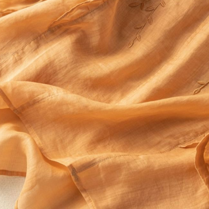 Detailed view of peach fabric with delicate leaf embroidery, highlighting the texture and stitchwork.