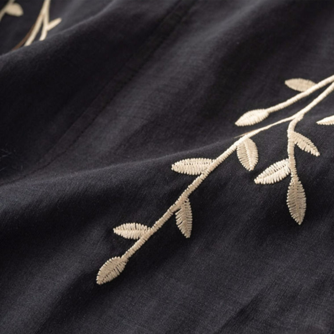 Close-up of a black fabric with intricate white leaf embroidery, showcasing fine stitch details and texture.