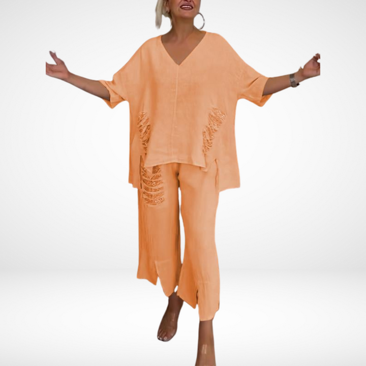 Model in pastel orange two-piece set, displaying open arms in a white studio setting.