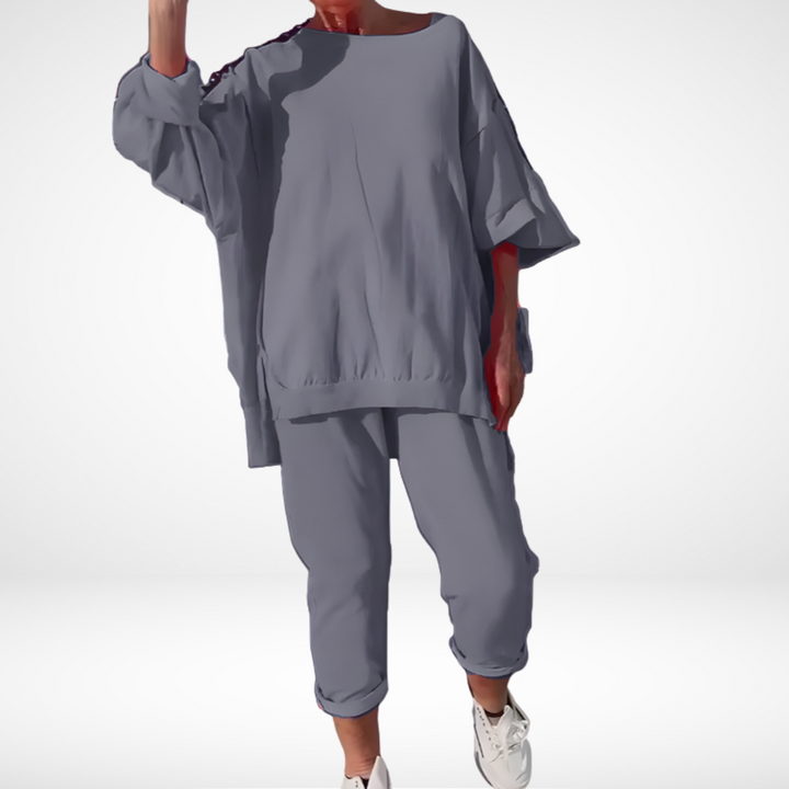 Muted gray comfort lounge set with loose-fitting top and cuffed pants, paired with casual sneakers in a studio.