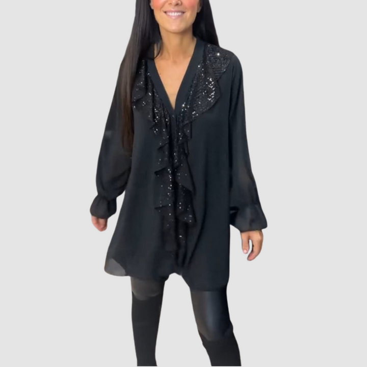 Black ruffled blouse with shimmering details, worn with black leggings in a studio setting.