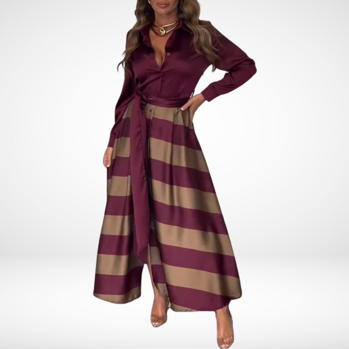 Woman wearing a burgundy and gold-striped maxi dress with long sleeves and a tied waist in a plain white studio.
