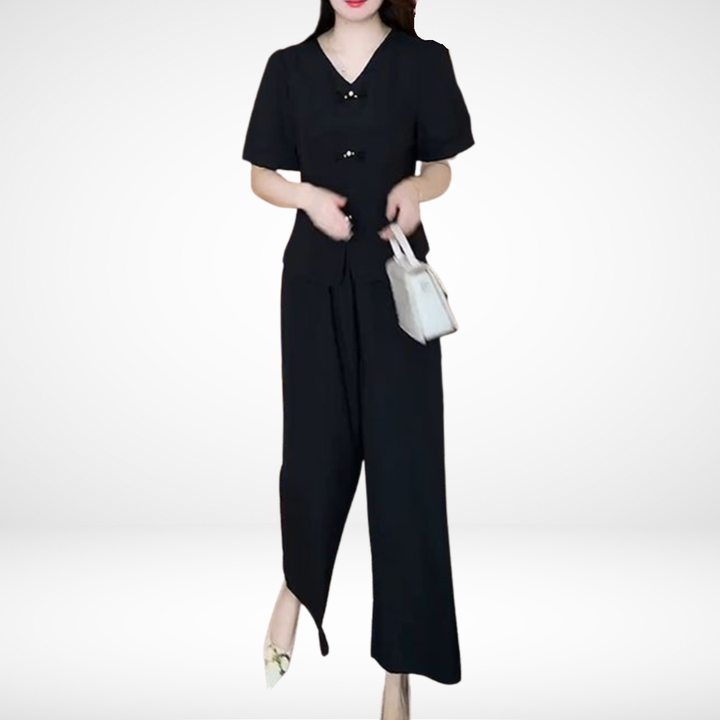 Model in black short-sleeve two-piece set, holding white bag, in white studio setting.
