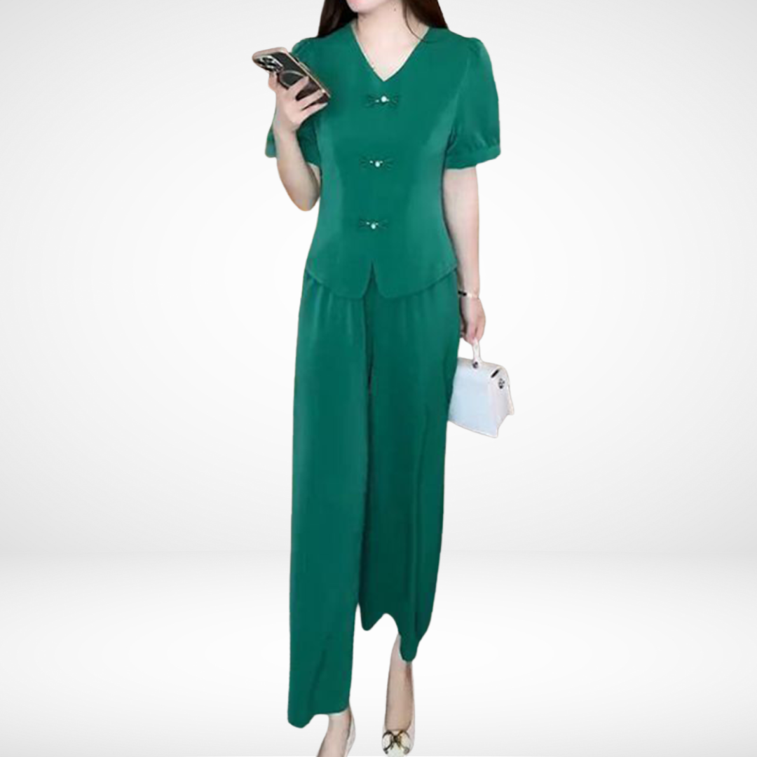 Model in green short-sleeve two-piece set, holding phone and white bag, against white studio background.