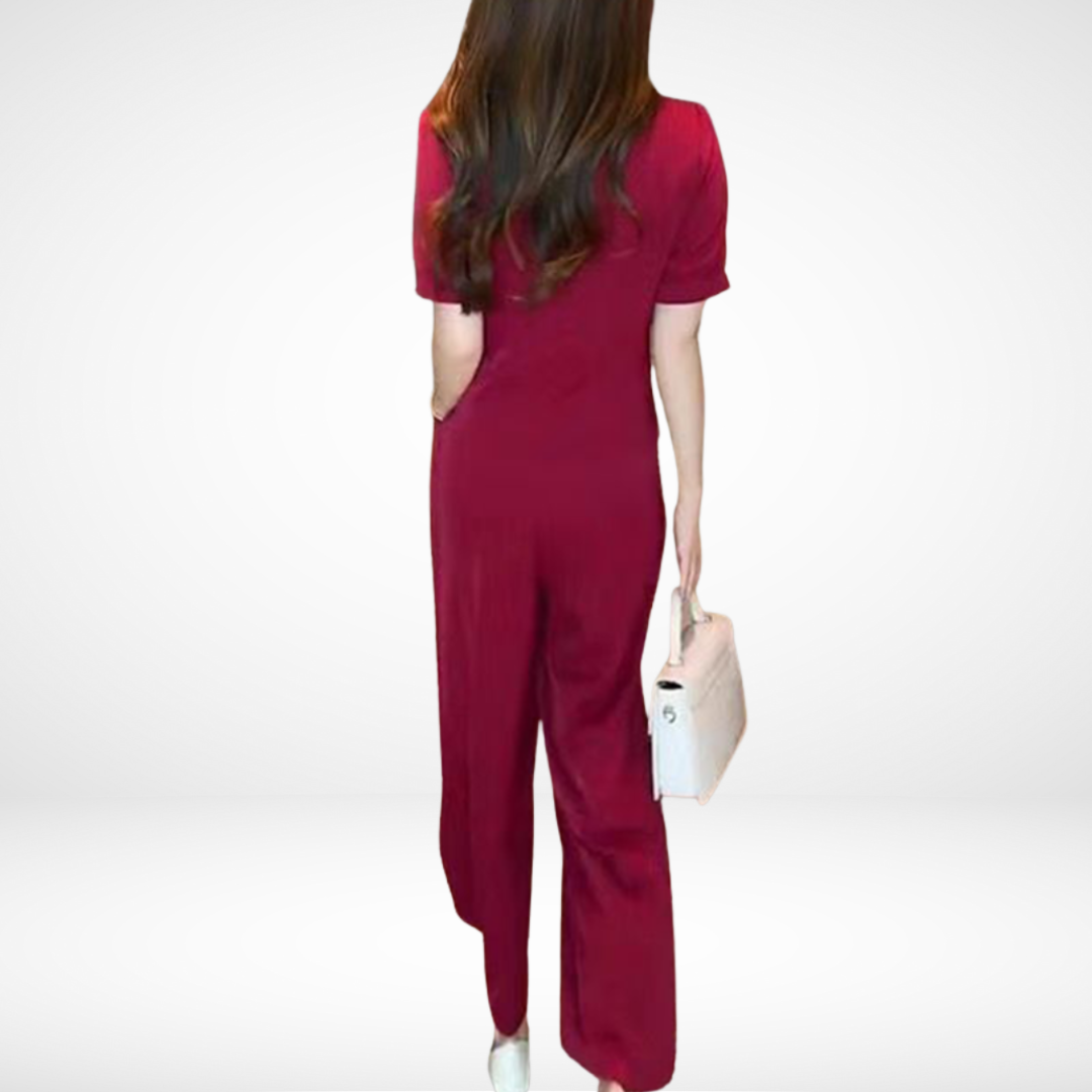 Back view of model in red short-sleeve two-piece set, holding white bag, in white studio setting.