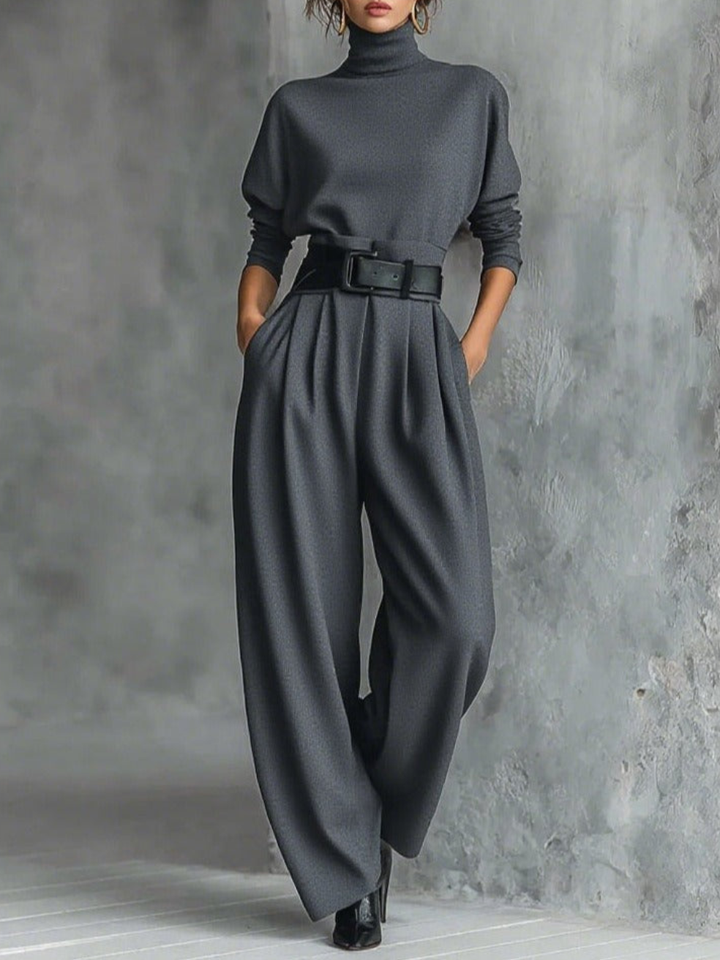 Model in a gray elegant top and straight-leg pants set with a belted waist, standing in a textured studio.