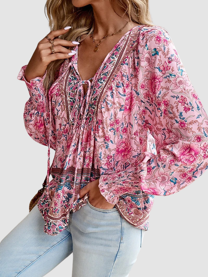 Side view of elegant floral blouse in pink hues with detailed patterns, paired with light denim jeans, on a gray backdrop.