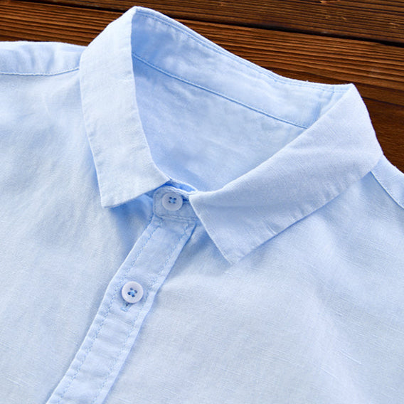 Close-up of light blue linen shirt collar and buttons on wooden surface.