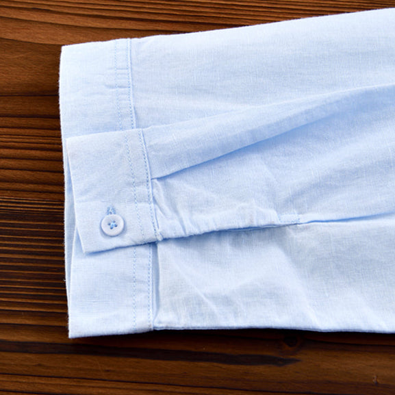 Light blue linen shirt sleeve with button detail on wooden surface.