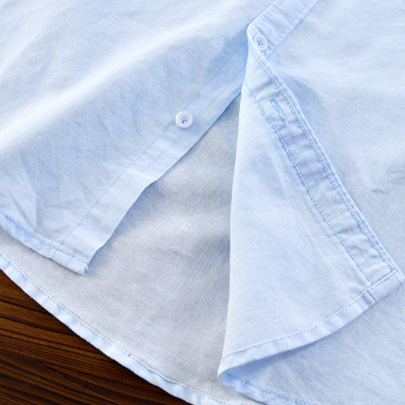 Detail of light blue linen shirt hem and buttons on wooden surface.
