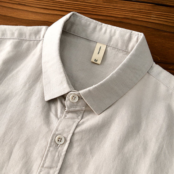 Close-up of light gray linen shirt collar and buttons on wooden surface.
