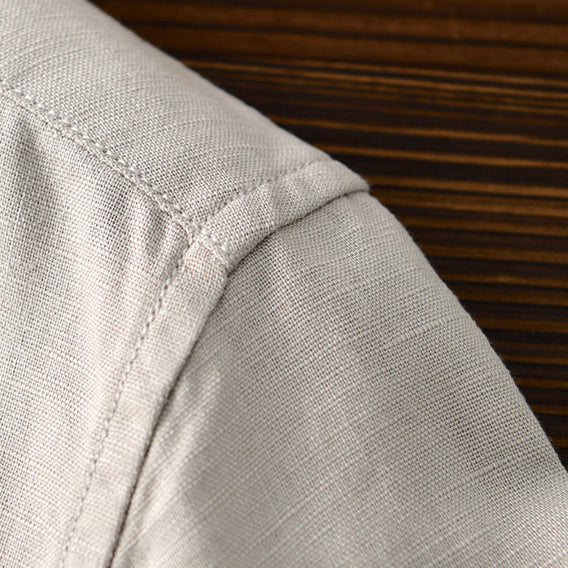 Detail of light gray linen shirt shoulder stitching on wooden surface.