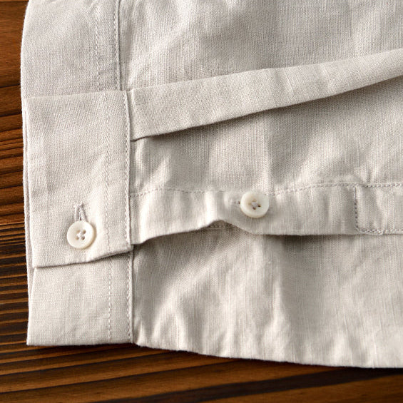Light gray linen shirt sleeve with buttons on wooden surface.