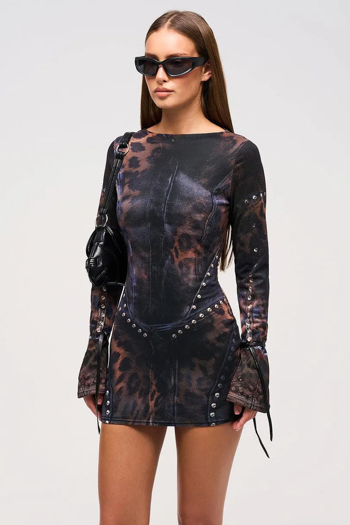 Model in black and brown patterned mini dress with studded details, holding a black bag, in a studio setting.