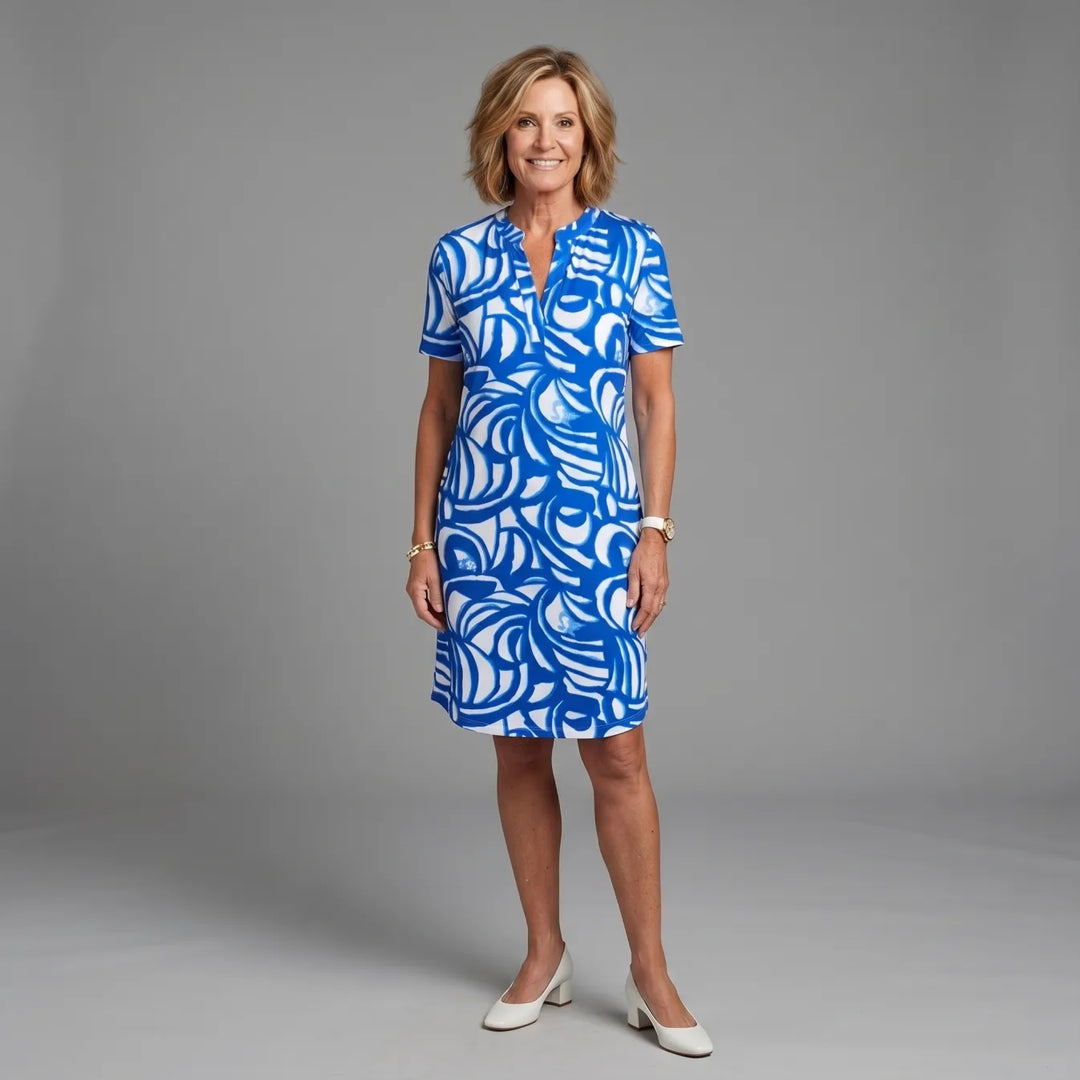Woman wearing a blue and white patterned summer dress in a studio setting, smiling.