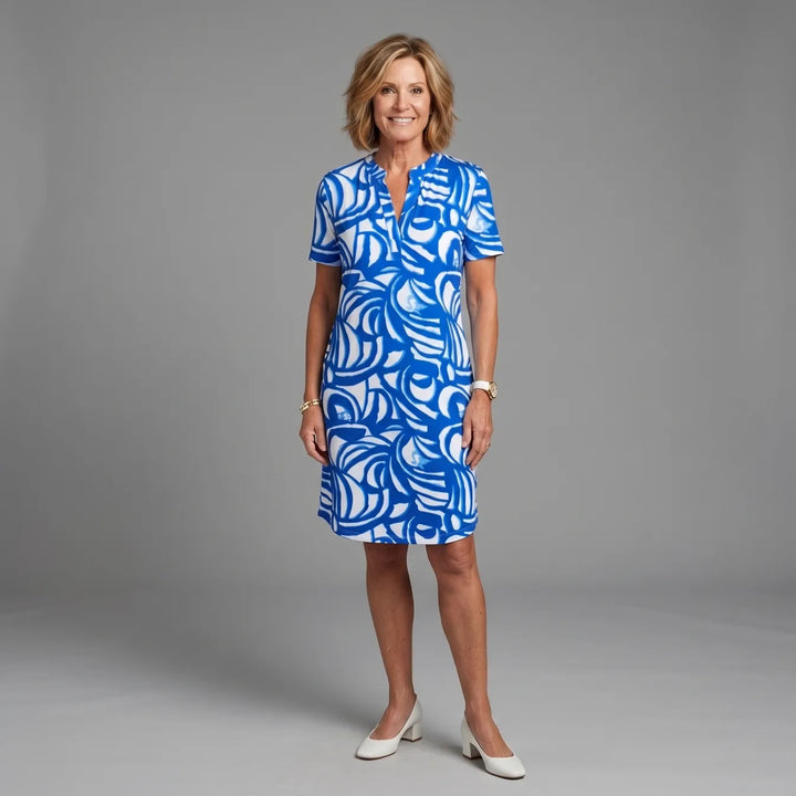 Woman wearing a blue and white patterned summer dress in a studio setting, smiling.