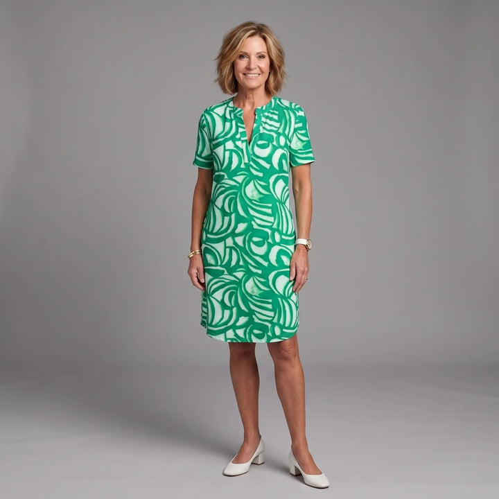 Woman wearing a green and white patterned summer dress in a studio setting, smiling.