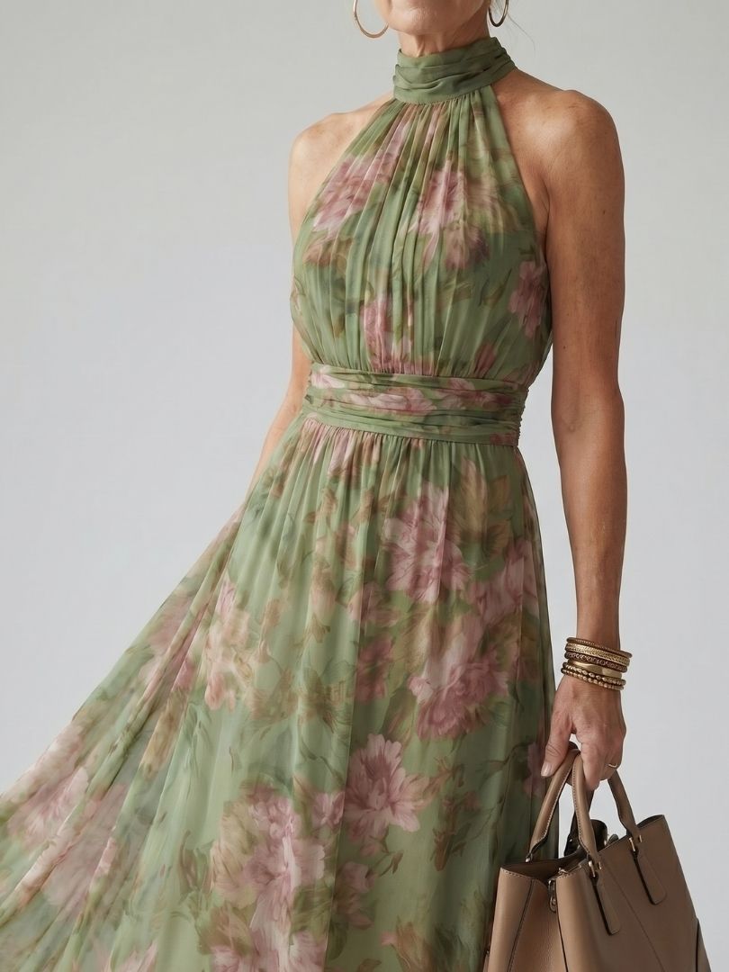 Close-up of green floral halter midi dress, model holding a beige handbag, studio backdrop.