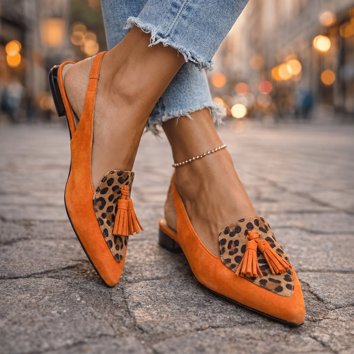 Orange sandals with leopard print and tassels, worn with frayed jeans, street background.