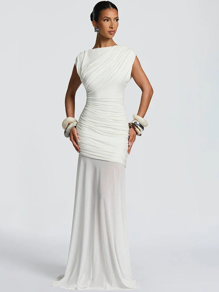 Elegant white gown with ruched details and sheer skirt, accessorized with chunky bracelets, in a studio setting.