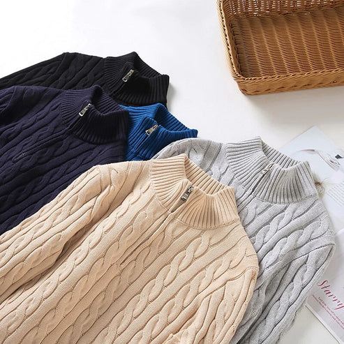 Collection of cable-knit half-zip sweaters in beige, gray, blue, navy, and black, arranged in a cascade on a white surface with a wicker basket.
