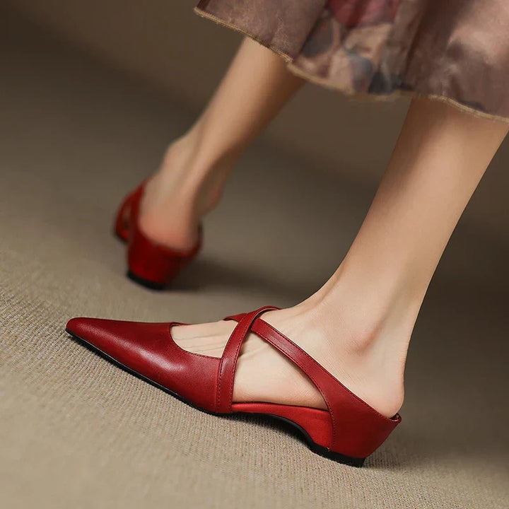 Red mules with criss-cross straps in a relaxed, raised foot position.