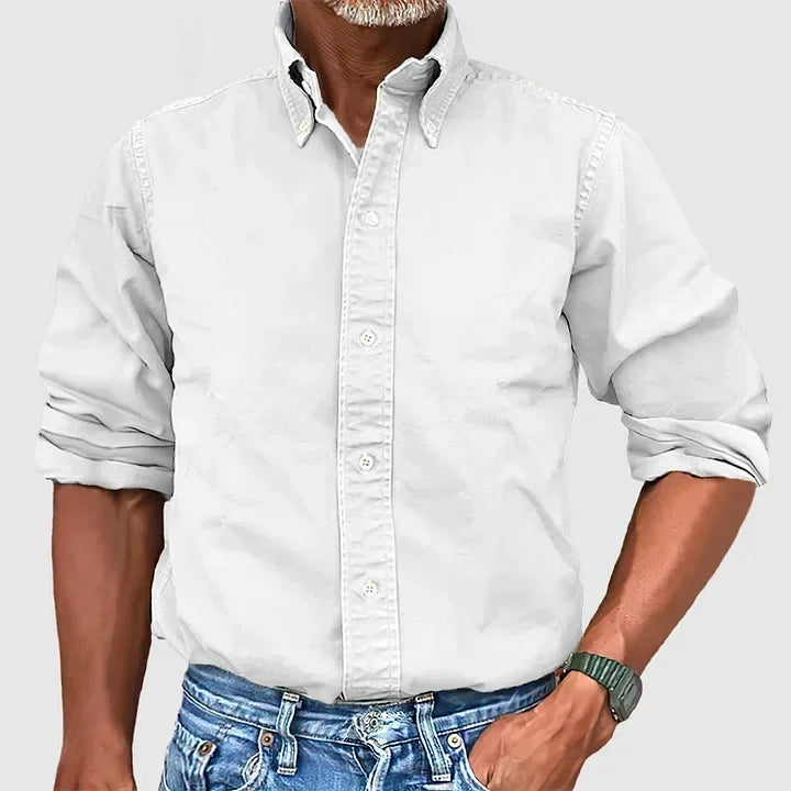 Man wearing a white button-up shirt with rolled sleeves and blue jeans against a plain gray background.