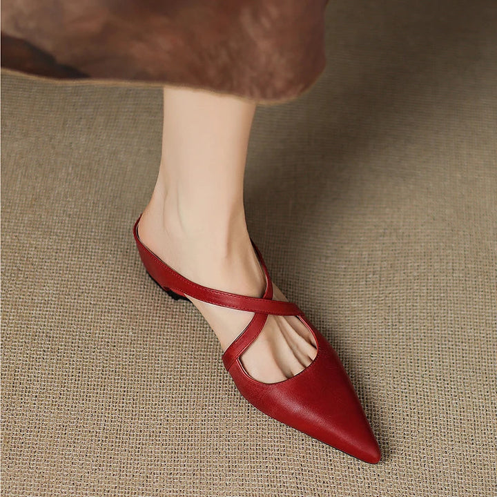 Person lifting foot slightly in red mules with criss-cross straps.