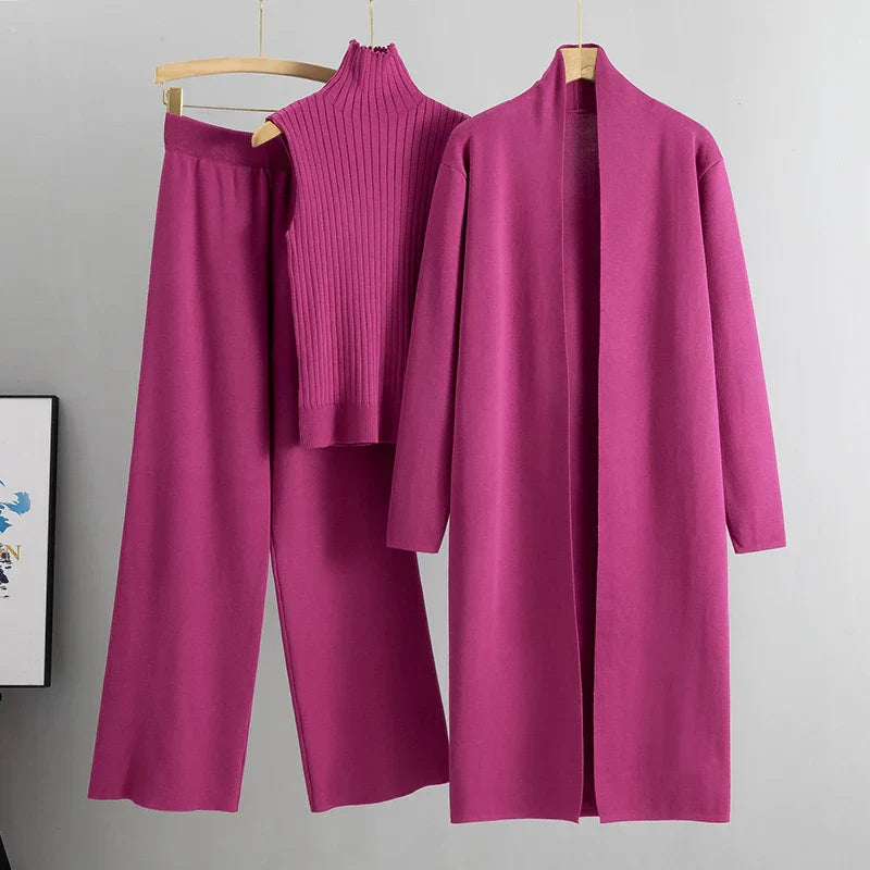 Bright pink three-piece set with sleeveless ribbed top, wide-leg pants, and long open cardigan on hangers in a studio setting.