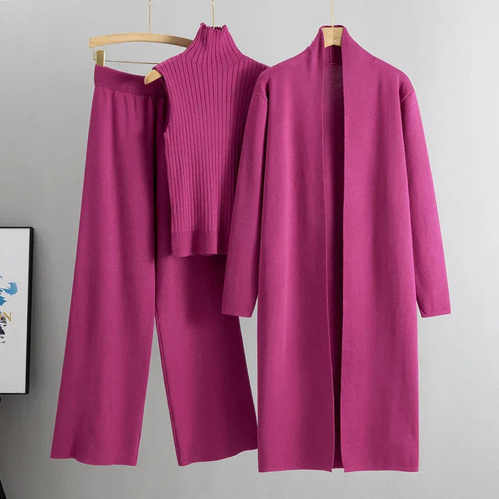 Bright pink three-piece set with sleeveless ribbed top, wide-leg pants, and long open cardigan on hangers in a studio setting.