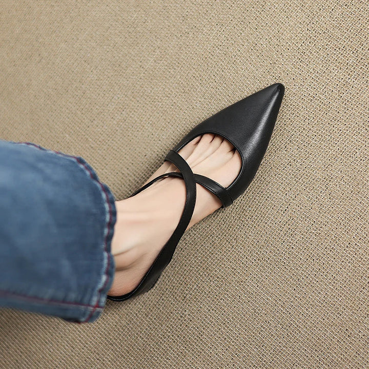 Black mules with foot stepping into one, paired with denim jeans.