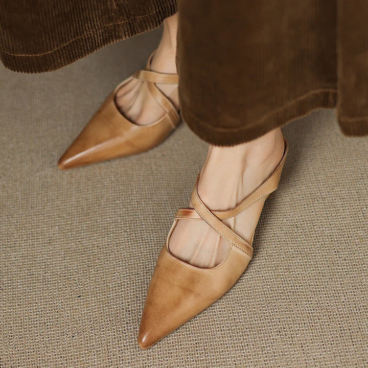 Person wearing tan mules with criss-cross straps under brown pants.
