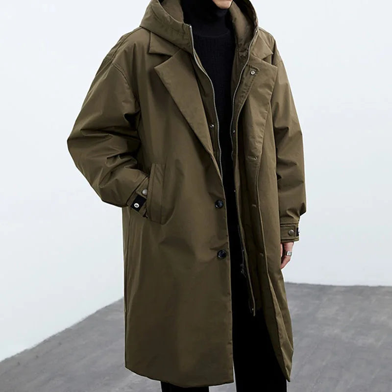 Person in a brown long coat with hood, standing in a gray studio.