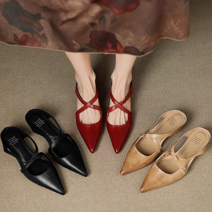 Red mules worn, black and tan mules beside on textured surface.