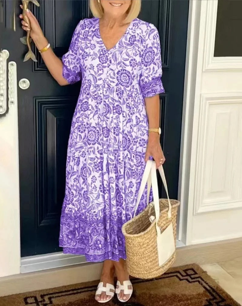 Woman wearing a purple floral V-neck dress with a straw bag, near a black door.
