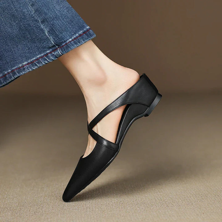 Black mules with criss-cross straps worn, foot slightly lifted.