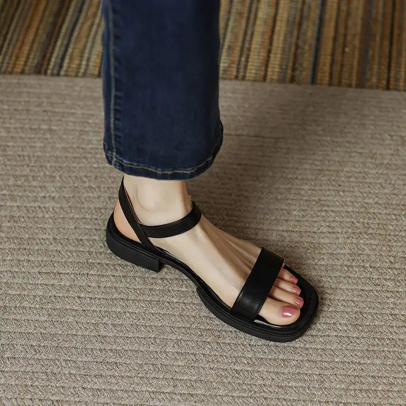 Black sandals on foot, textured surface, wearing blue jeans.