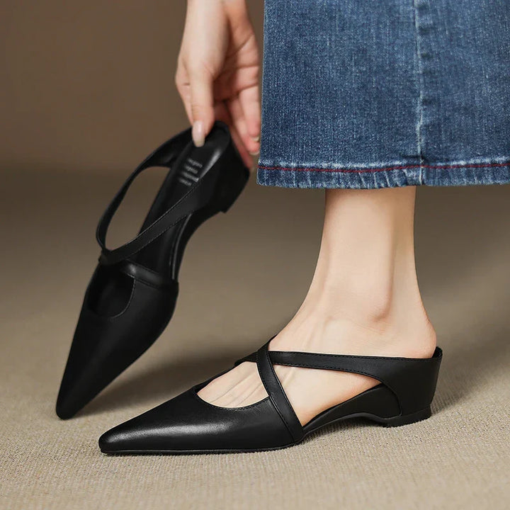 Person holding a black mule, wearing one with denim jeans.