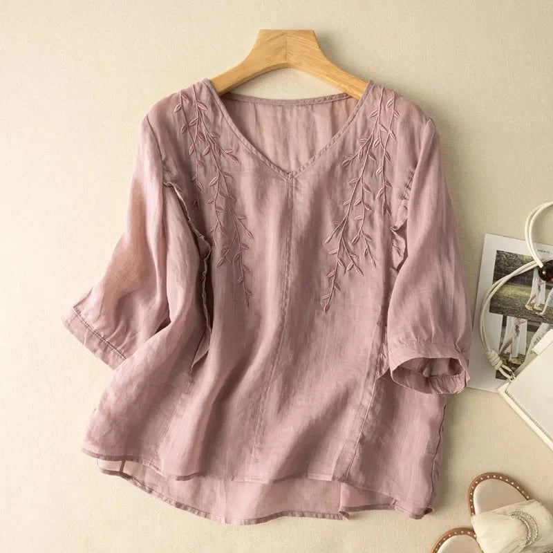 Mauve loose retro top with elegant leaf embroidery, displayed on a wooden hanger against a neutral wall with sandals and bag.