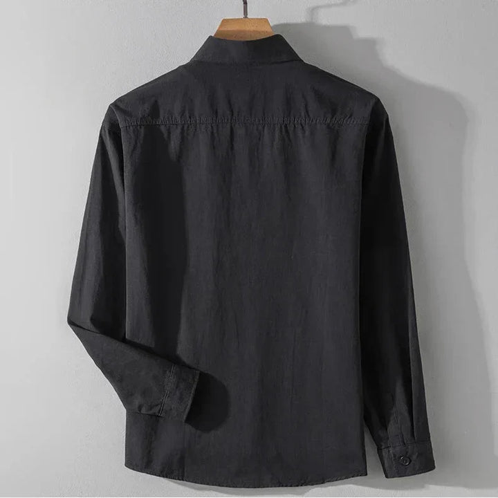Back view of dark charcoal shirt with long sleeves on wooden hanger, gray studio background.