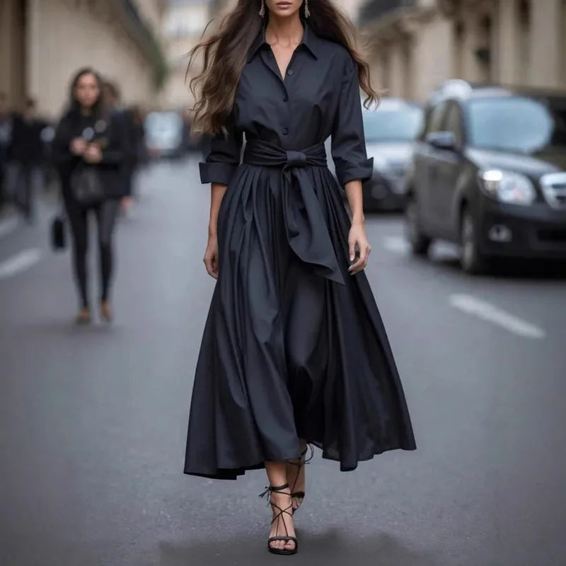 Chic black maxi dress with a cinched waist and loose sleeves, styled with black strappy heels on a city street.