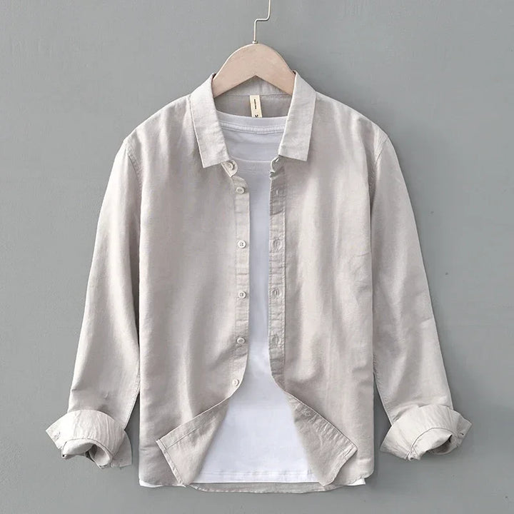 Light gray linen shirt with rolled sleeves on hanger, against gray wall.