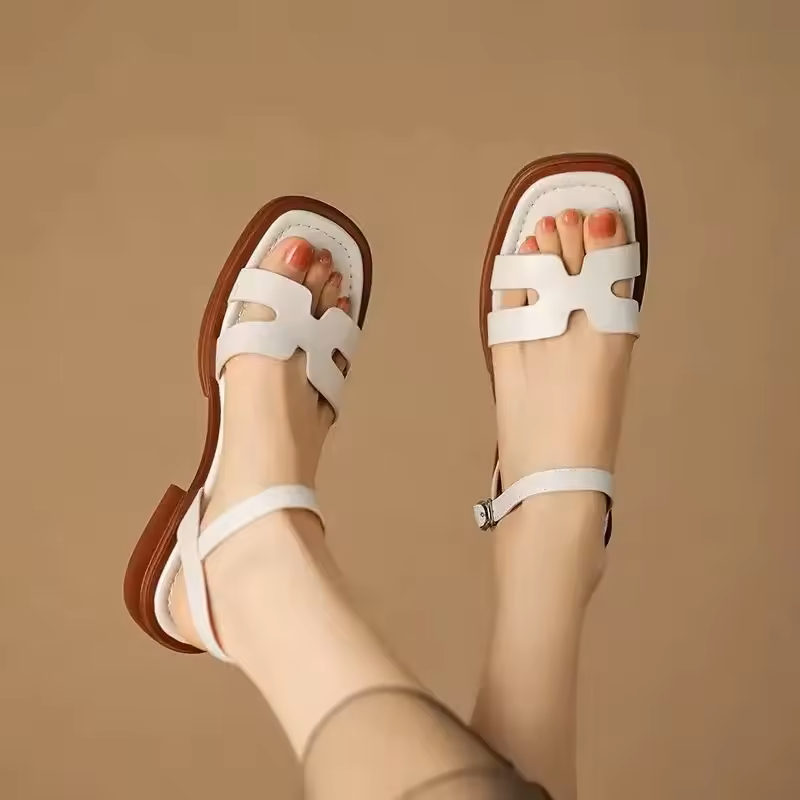White Roman-style sandals with ankle strap, showcased against a beige background indoors.