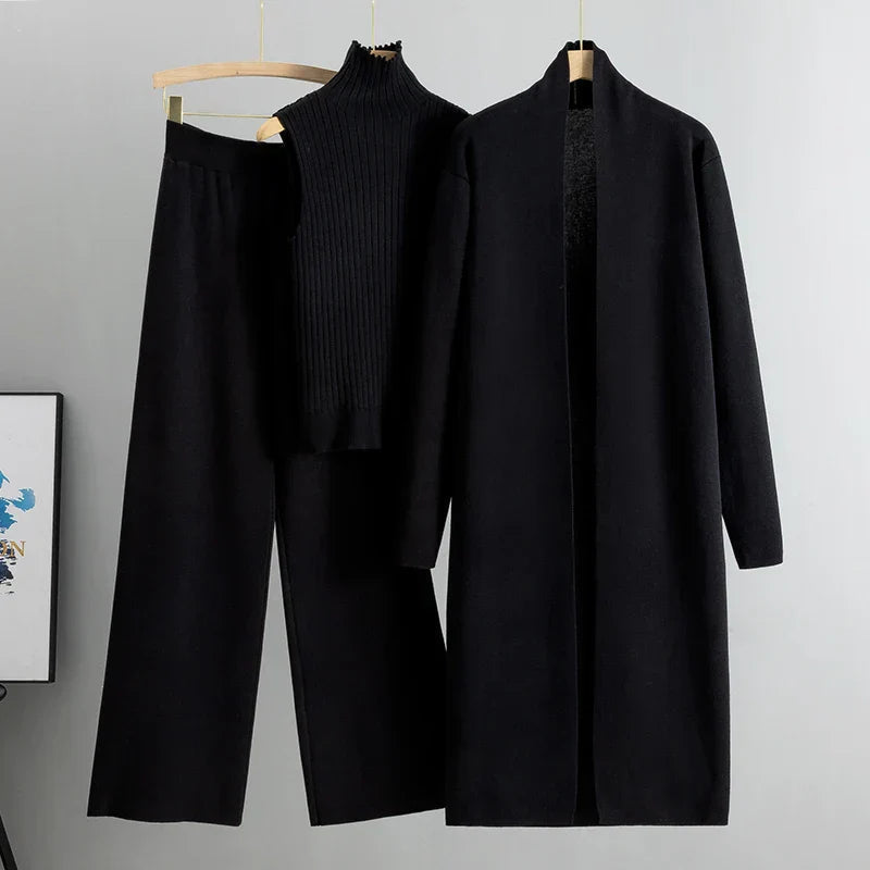 Black three-piece set including sleeveless ribbed top, wide-leg pants, and long open cardigan on hangers in a studio setting.