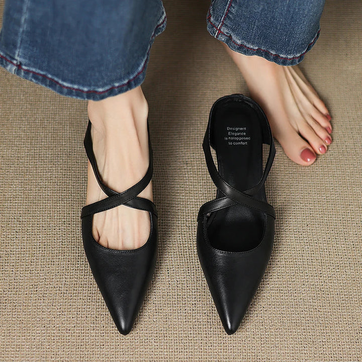 Person standing barefoot next to worn black mule on carpet.
