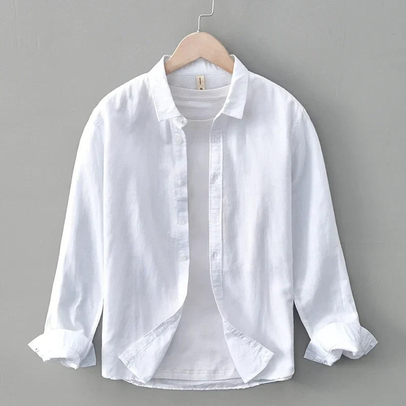White linen shirt with rolled sleeves on hanger, against gray wall.