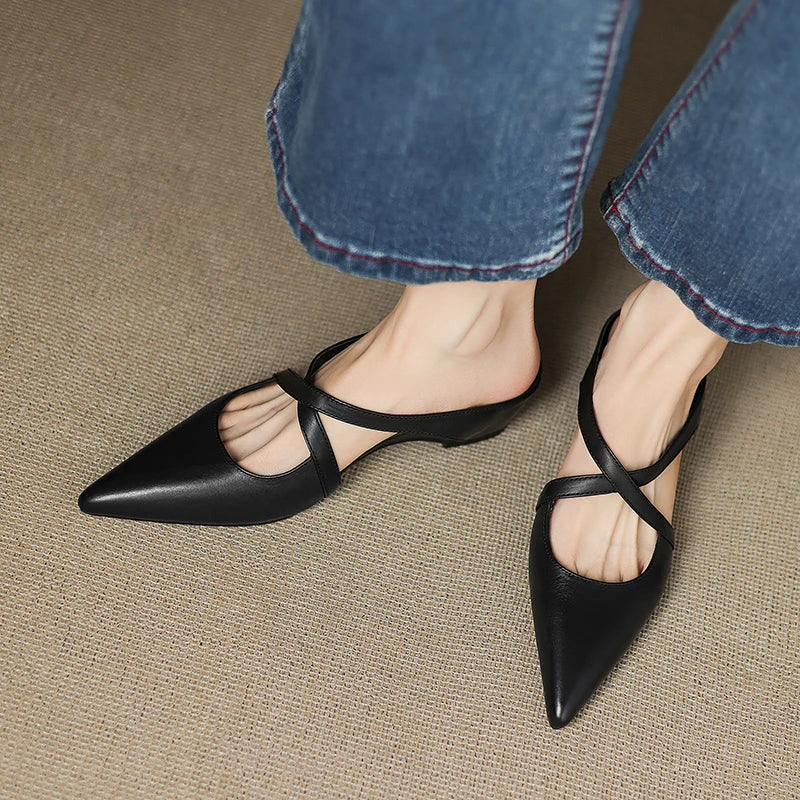 Top view of black mules with criss-cross straps worn with denim jeans.