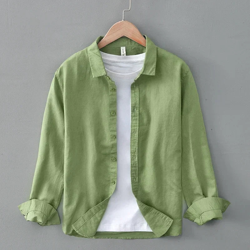 Green linen shirt with rolled sleeves on hanger, against gray wall.